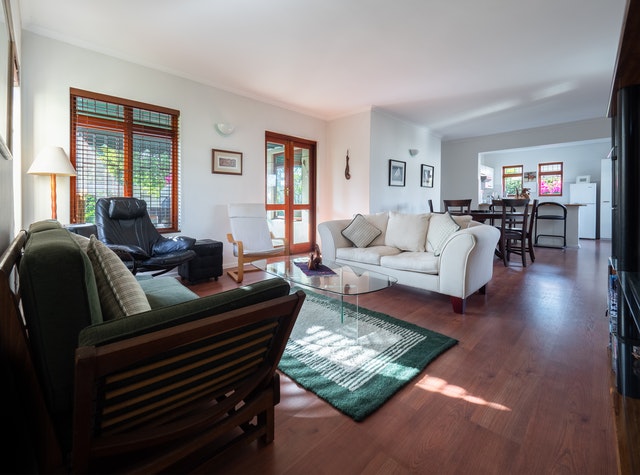 a living room with dark flooring large windows and mismatched furniture